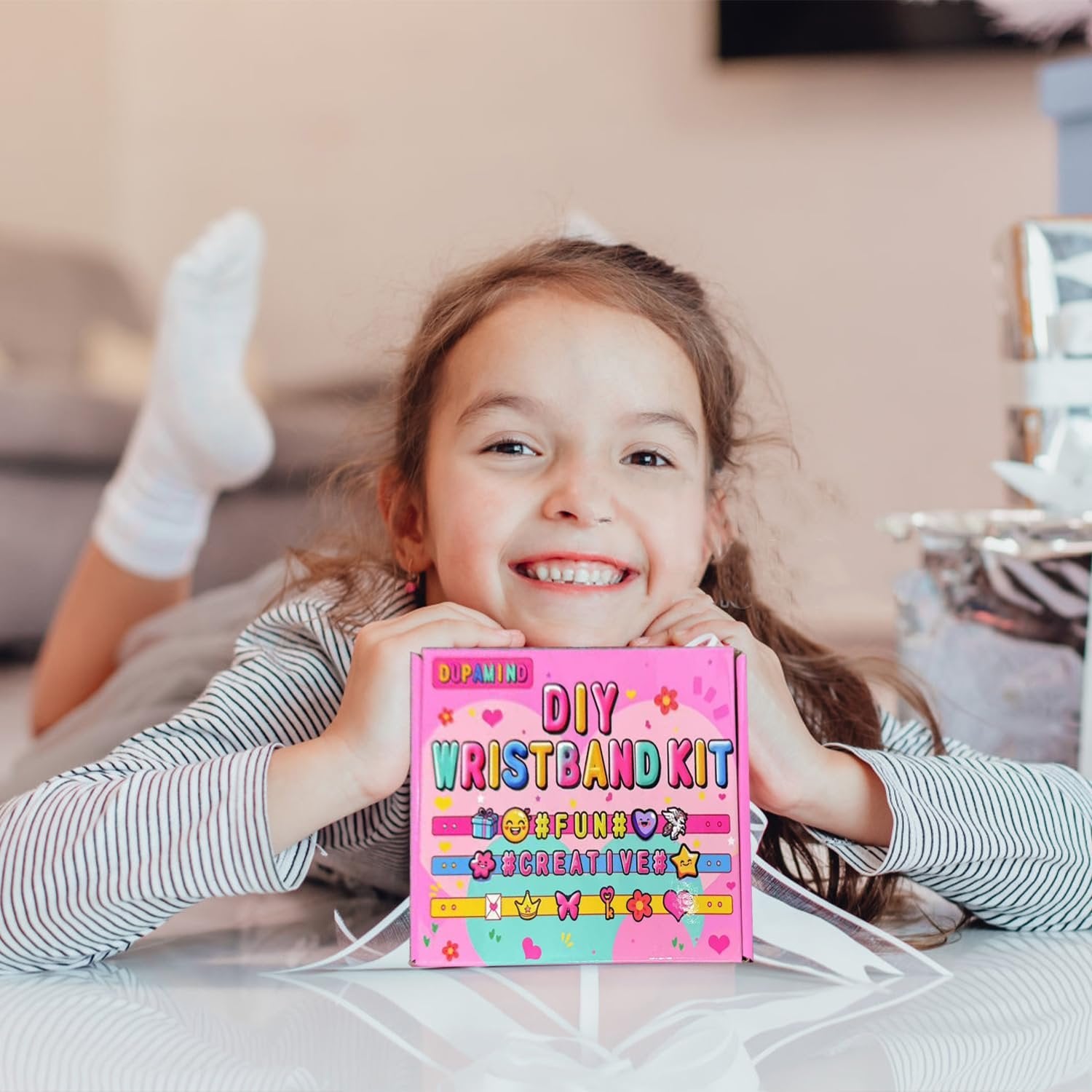 Smiling girl holding a pink DIY wristband kit box with colorful designs and text.