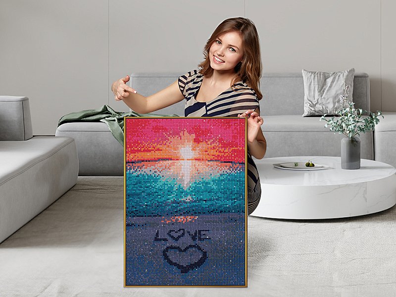 Woman holding a completed diamond painting kit of a beach sunset with the word LOVE and a heart on the sand.