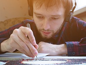 Man with headphones doing a diamond painting kit, focusing on placing a rhinestone