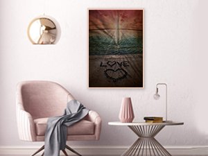 Diamond painting kit showing a beach sunset scene with the word LOVE written in the sand in a heart shape, framed on a wall.