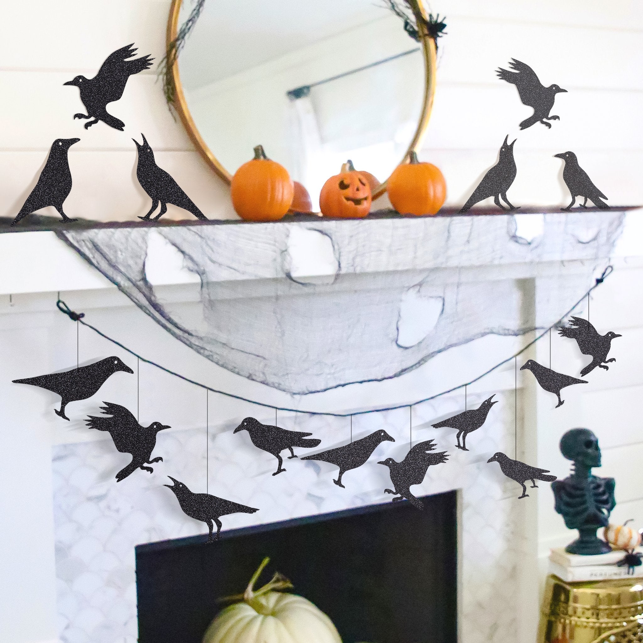 Glitter black crow garland hanging across a fireplace mantel with pumpkins and a skeleton decoration