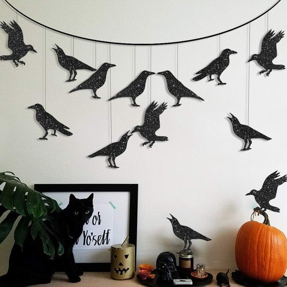 Glitter black crow garland hanging on a wall with a black cat, pumpkin, and Halloween decorations below.