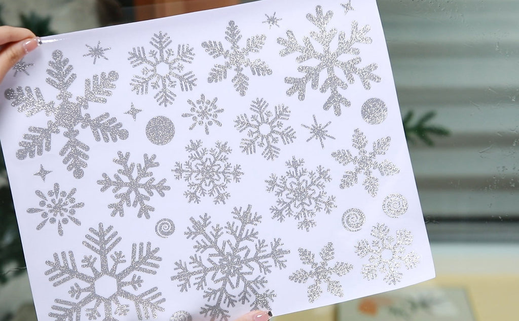 Sheet of silver glitter snowflake window clings, showing various sizes and designs of snowflakes and swirls.