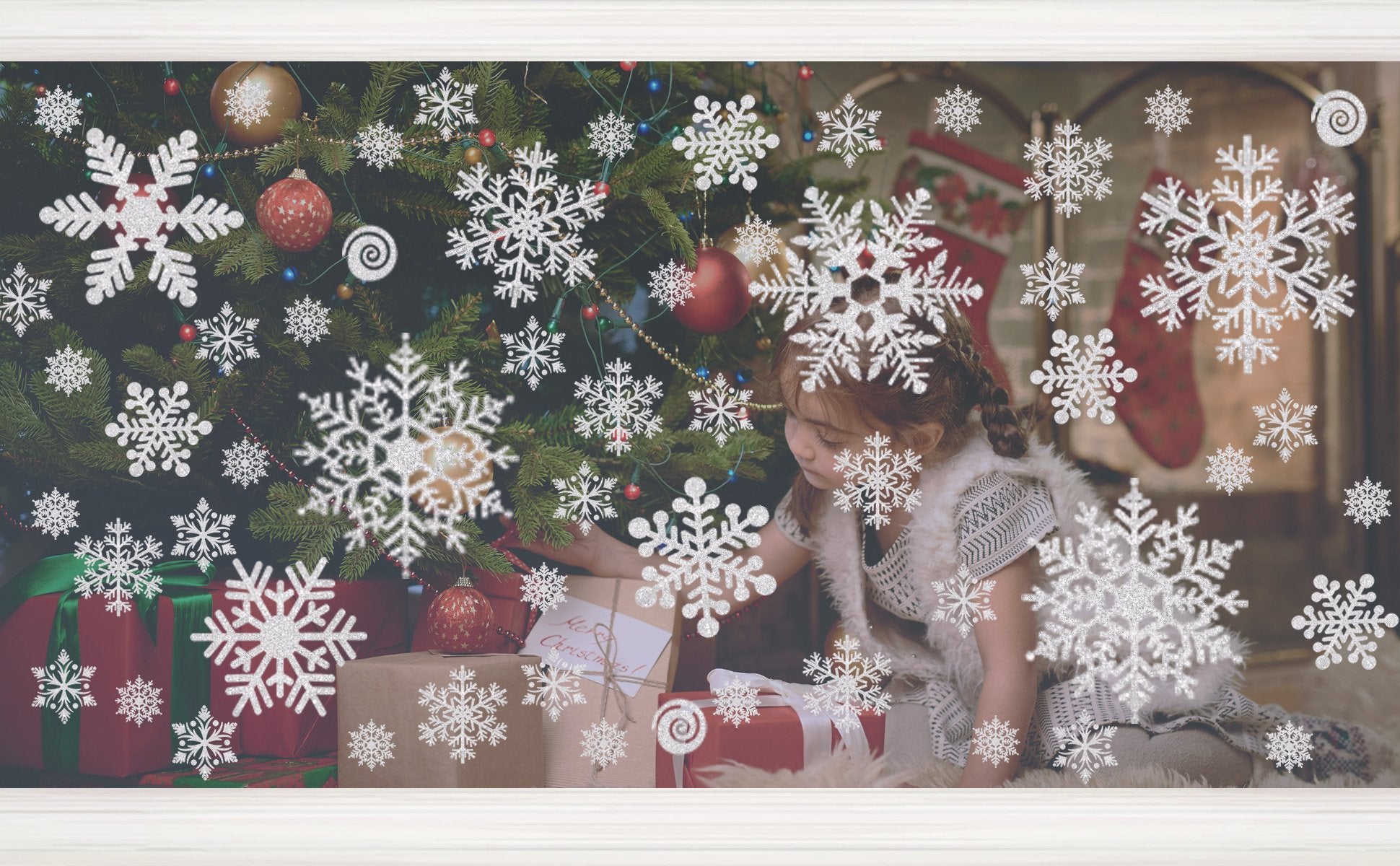 Glitter snowflake window clings applied to a window with a Christmas tree and gifts visible behind them.