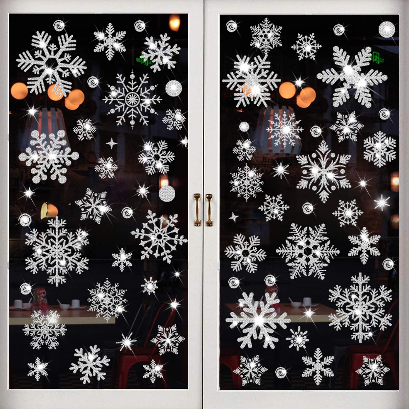 Glitter snowflake window clings applied to a glass door, showing various sizes and sparkling details against a dark background with interior lights visible.