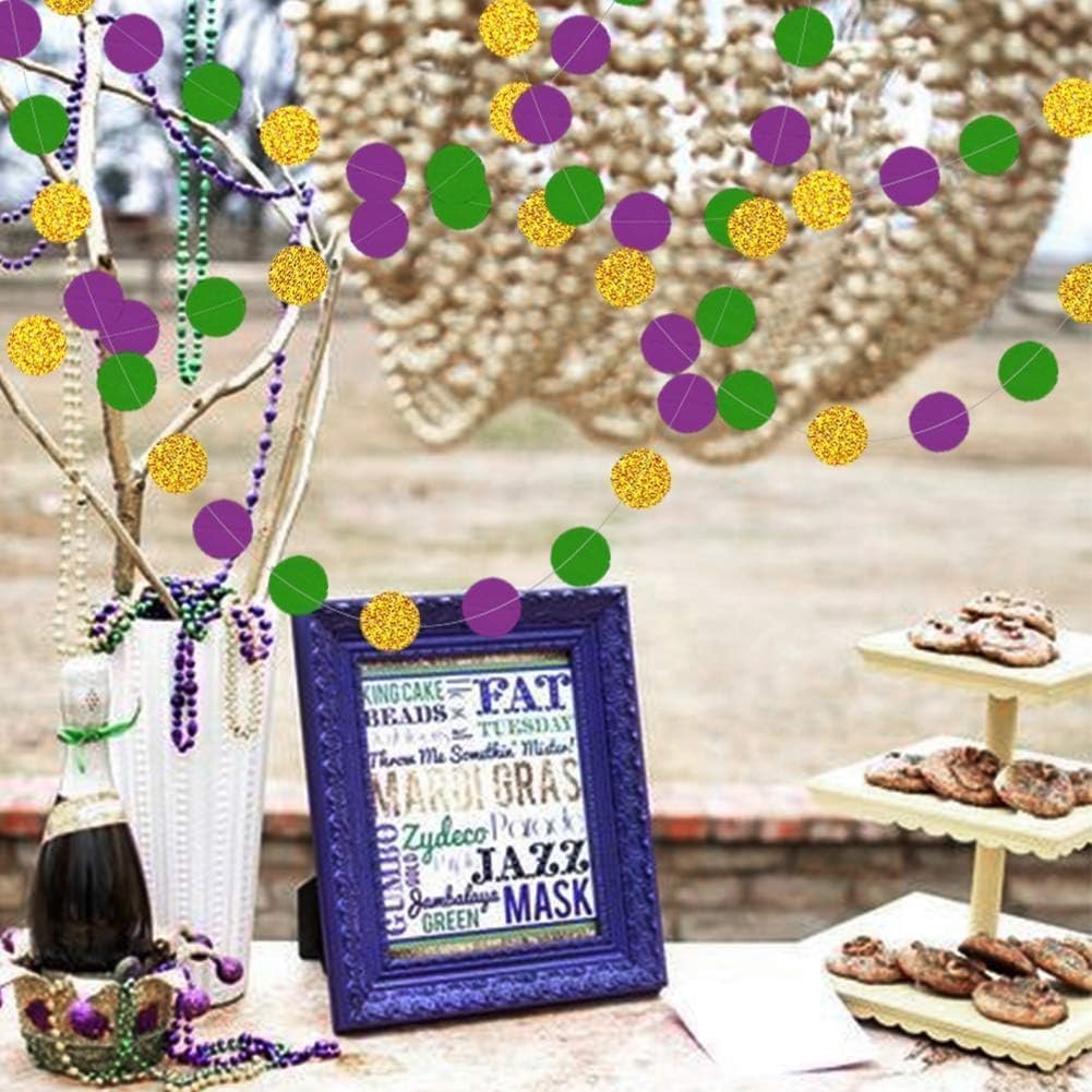 Mardi Gras themed party decorations with gold, purple, and green glitter circle garlands hanging above a table with a framed sign, beaded necklaces, and cookies.