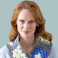 Woman with auburn hair wearing a crocheted granny square cowl in blue, white, and green