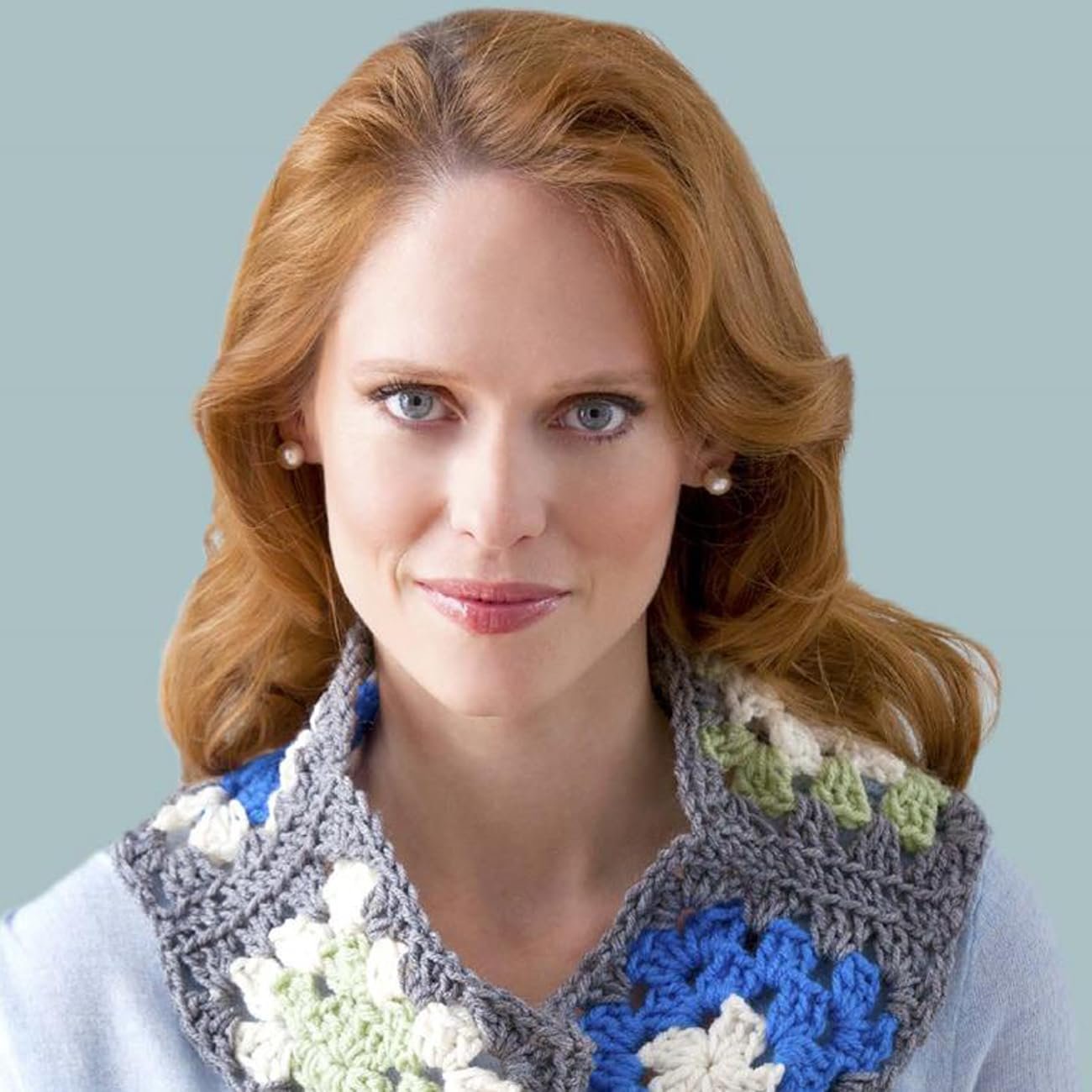 Woman with auburn hair wearing a crocheted granny square cowl in blue, white, and green