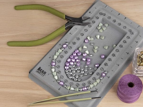 Grey flocked jewelry bead board with beads, pliers, tweezers, and thread for crafting