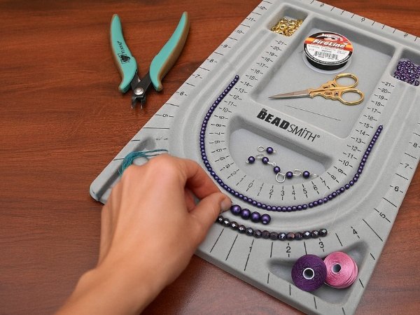 Grey flocked jewelry bead board with cover, showing beads, scissors, thread, and pliers.