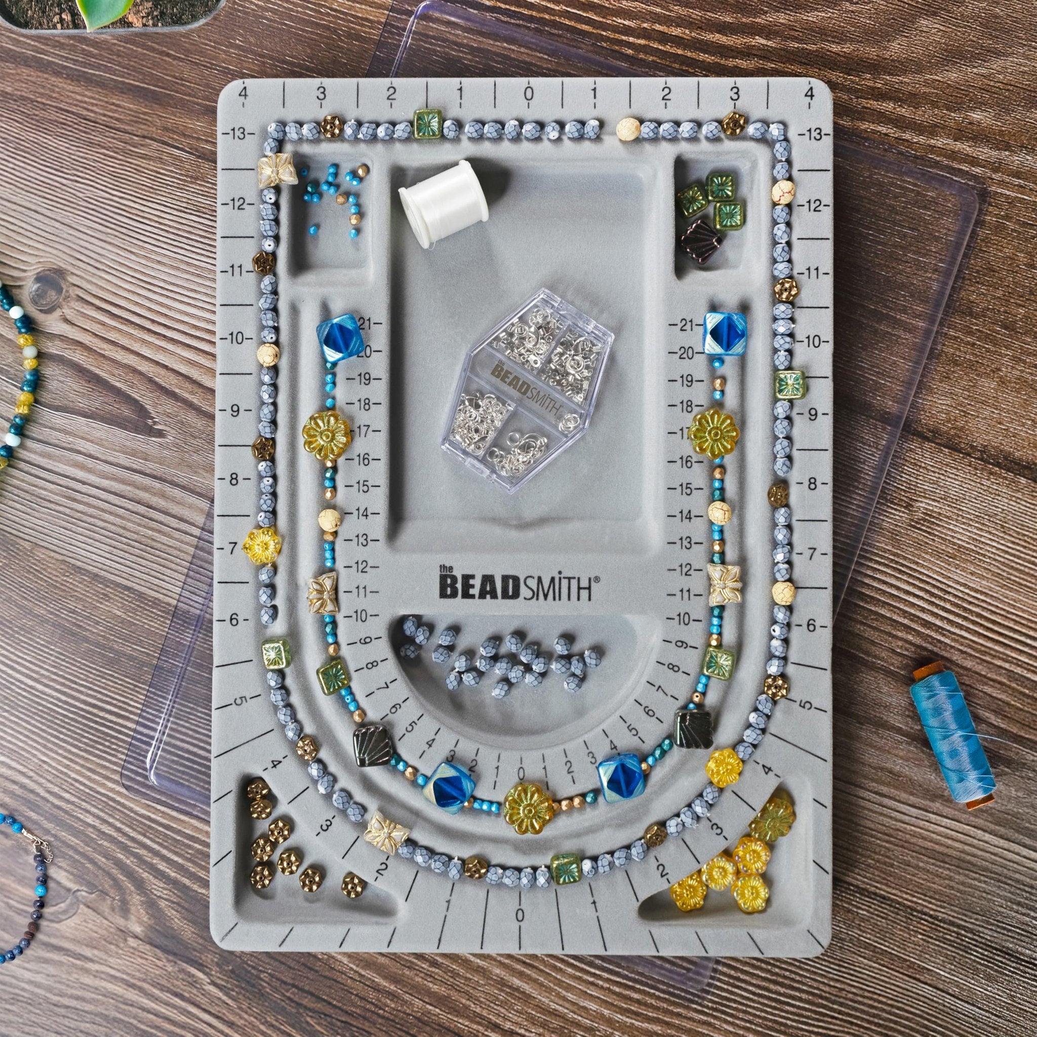 Grey flocked jewelry bead board with beads and findings arranged on it, top-down view. Logo is visible on the board.