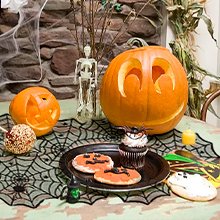 Halloween table setting with carved pumpkins, cookies, cupcake, and spider web table runner.