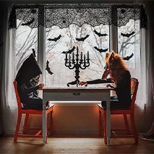 Halloween table setting with lace spider web valance, bats on window, and two figures seated at a table.