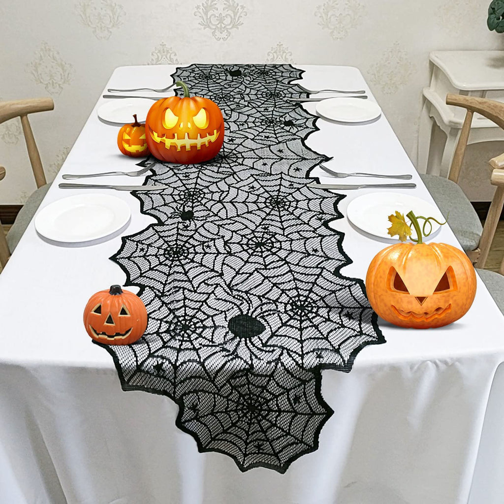 Halloween black lace spider web table runner on a white tablecloth with carved pumpkins and place settings.