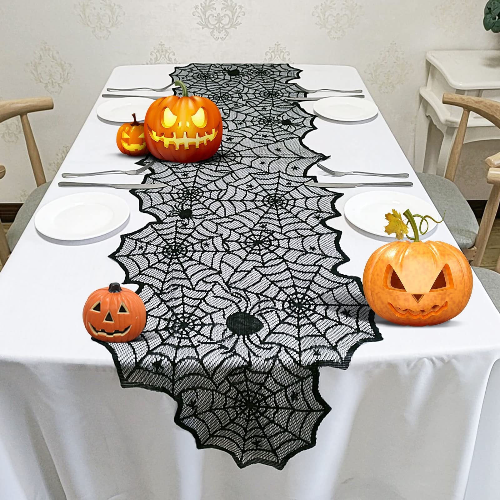Halloween black lace spider web table runner on a white tablecloth with carved pumpkins and place settings.