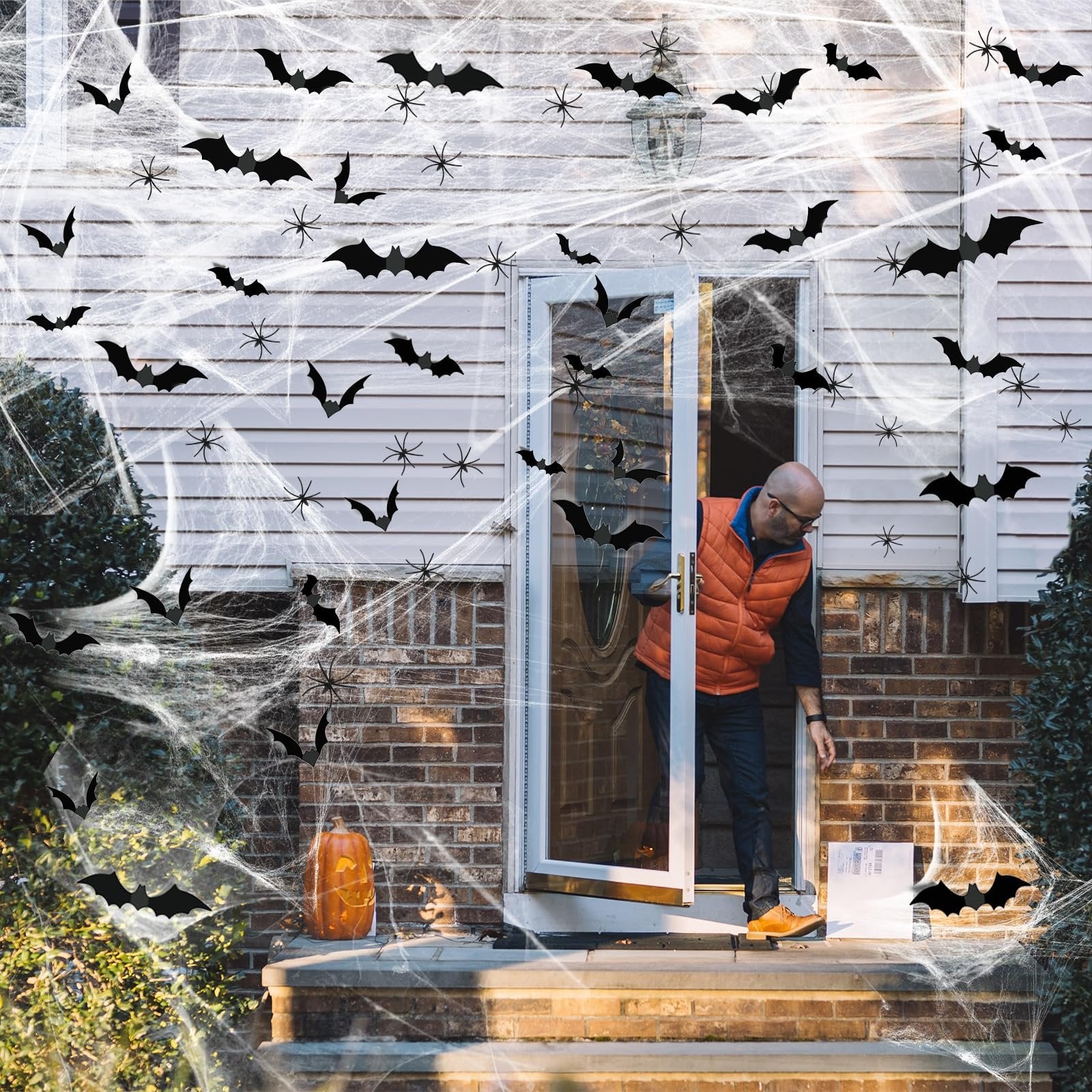 Man opening front door decorated with fake spider webs, bats, and spiders for Halloween