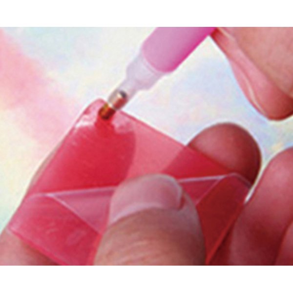 Close-up of hands using a diamond art applicator tool to place a diamond onto a pink acrylic ornament.
