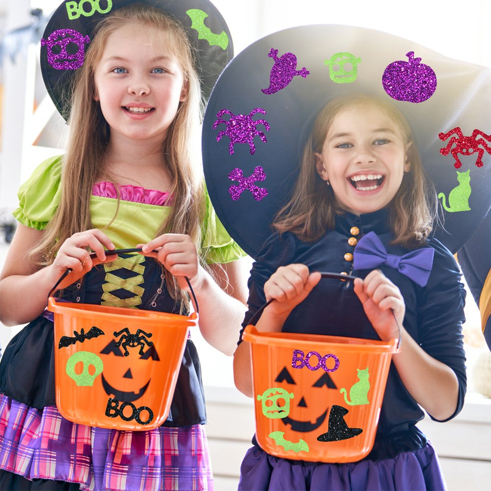Two smiling girls in Halloween costumes holding candy buckets decorated with glitter stickers.
