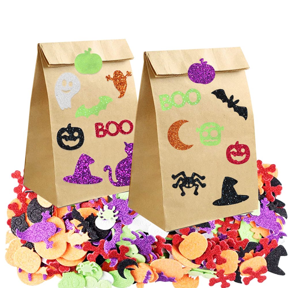Two brown paper bags decorated with glitter Halloween shapes and the word BOO, surrounded by a pile of assorted glitter foam stickers.