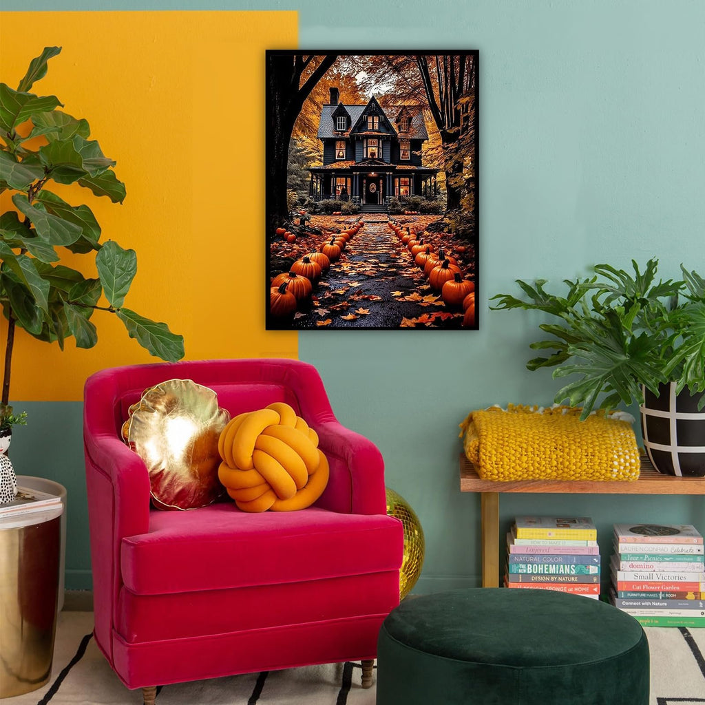Framed painting of a haunted house on a path lined with pumpkins and autumn leaves, displayed in a room with a pink chair.
