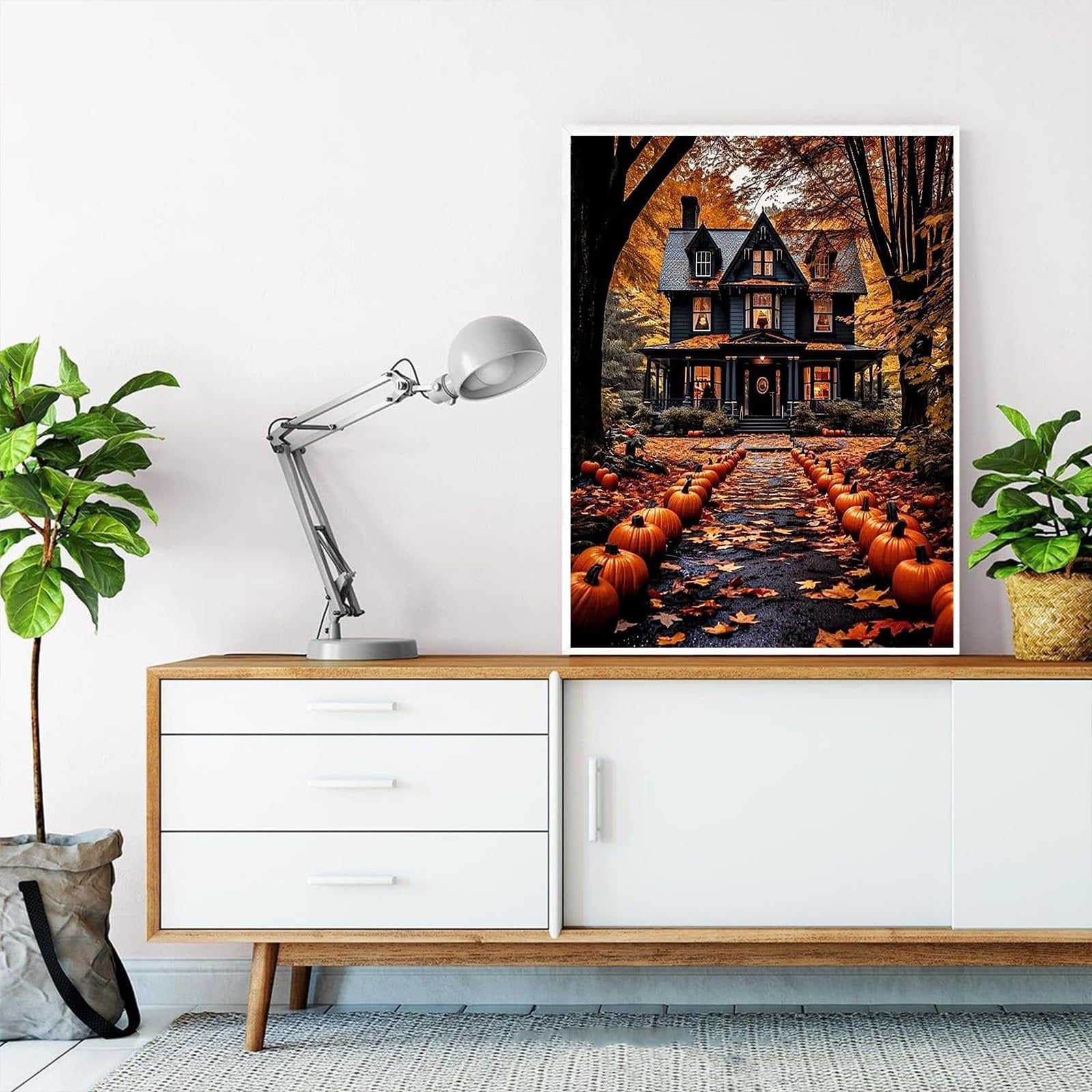 Halloween house with pumpkins and autumn leaves on path, displayed on a wall above a cabinet.