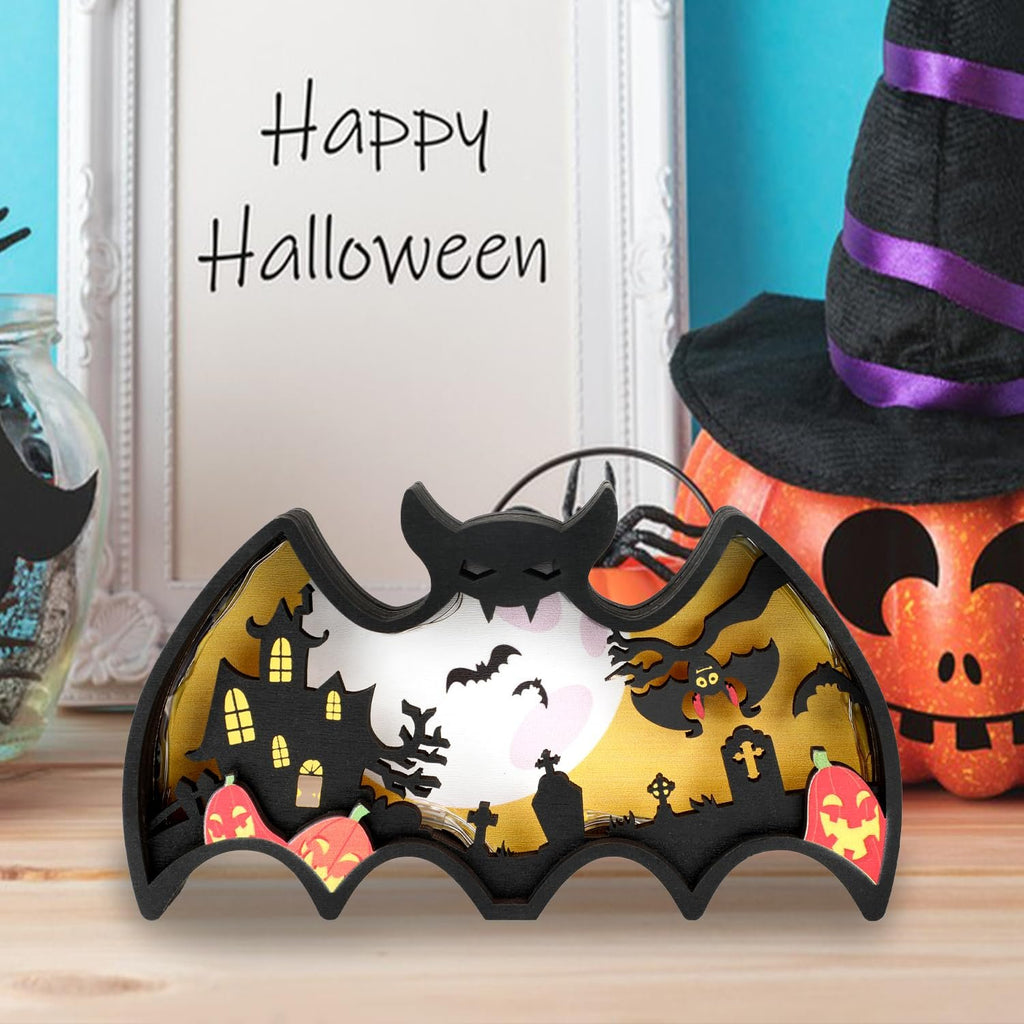 Halloween light-up bat shadow box with haunted house, pumpkins, and bats, on a wooden table.