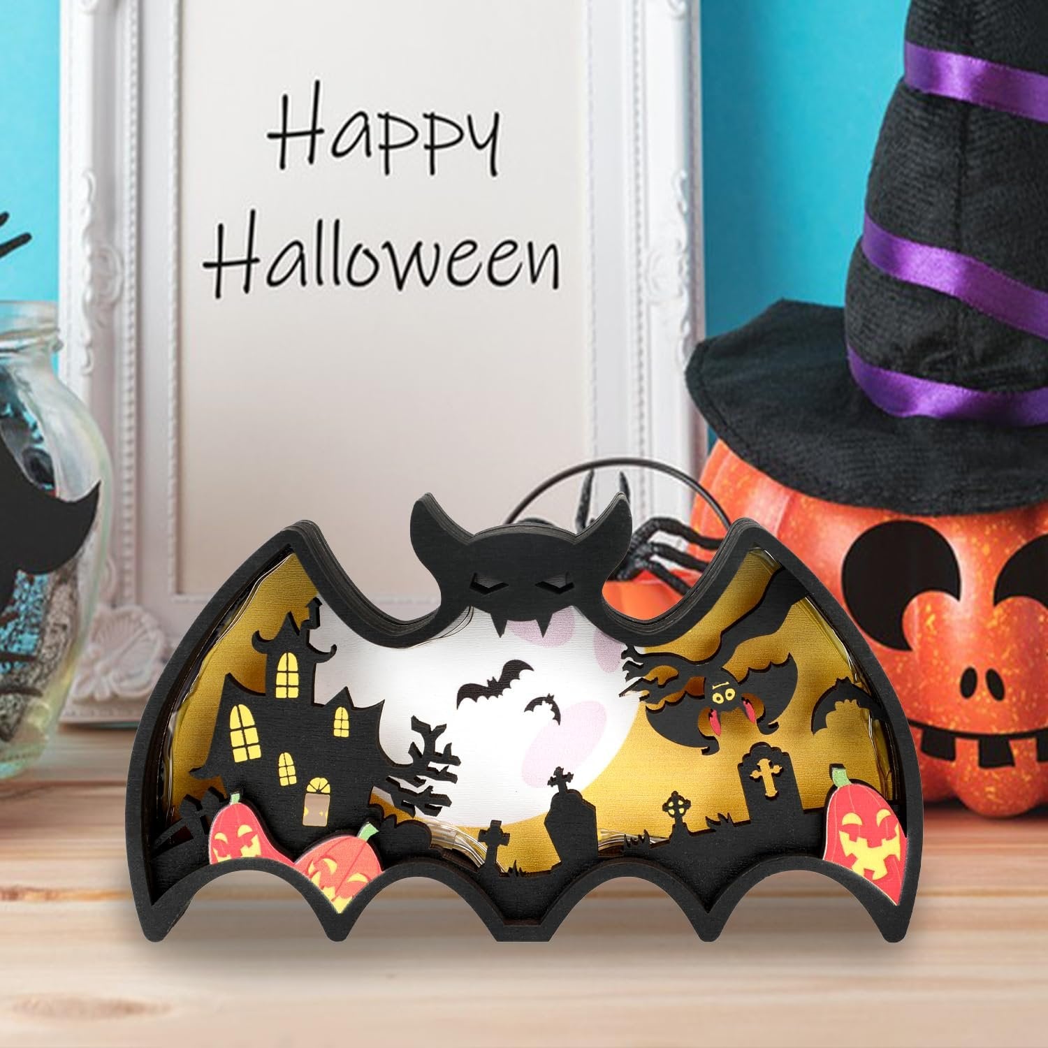Halloween light-up bat shadow box with haunted house, pumpkins, and bats, on a wooden table.