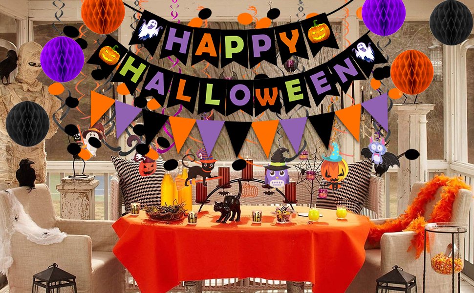 Halloween party decorations including a 'Happy Halloween' banner, honeycomb balls, bunting, and themed cutouts on a table and chairs.