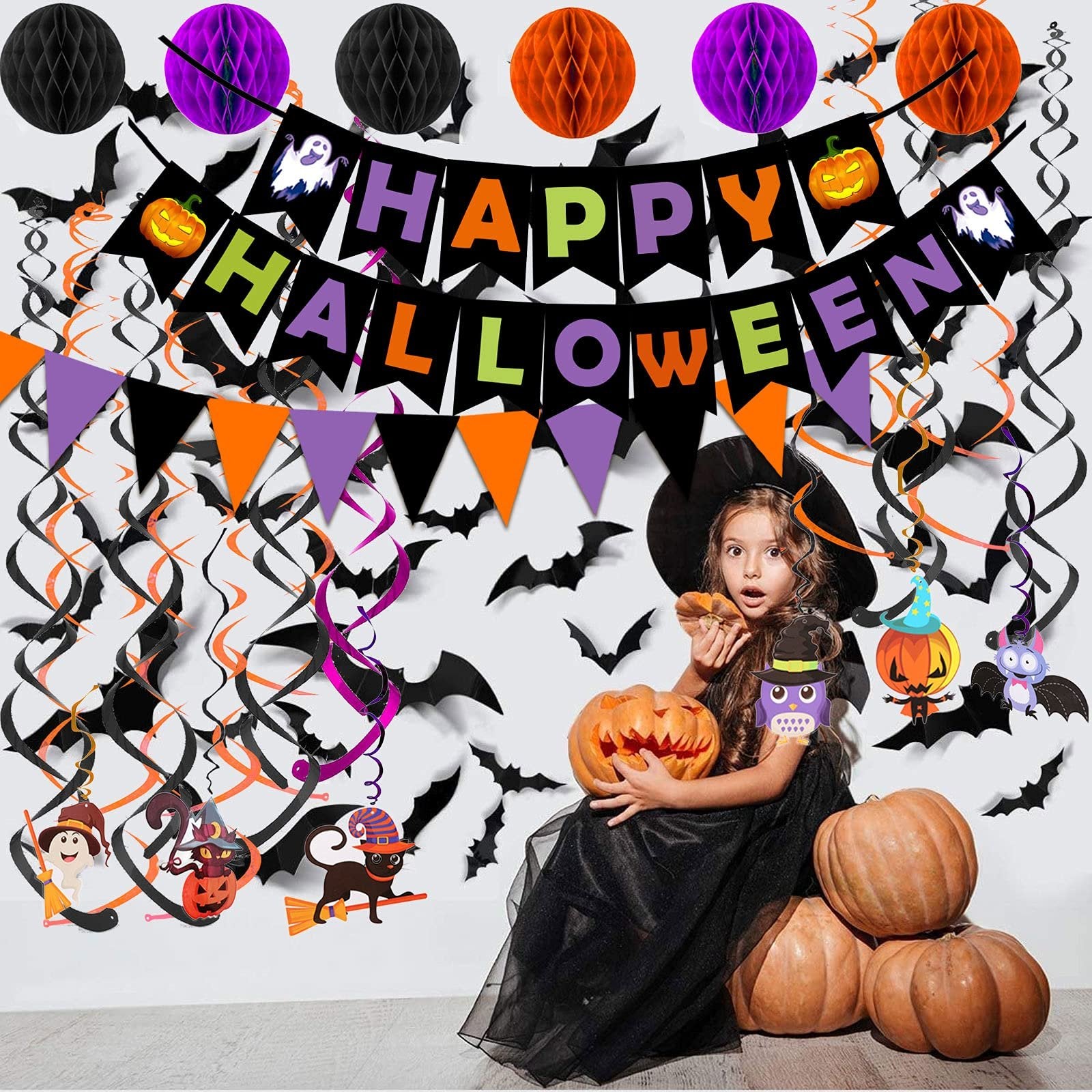 Girl in witch costume holding pumpkin with Halloween decorations including banner, honeycomb balls, and swirling streamers