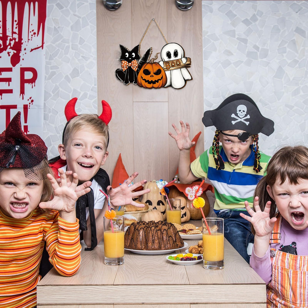 Four children in Halloween costumes at a table with a wooden hanging sign featuring a black cat, pumpkin, and ghost.