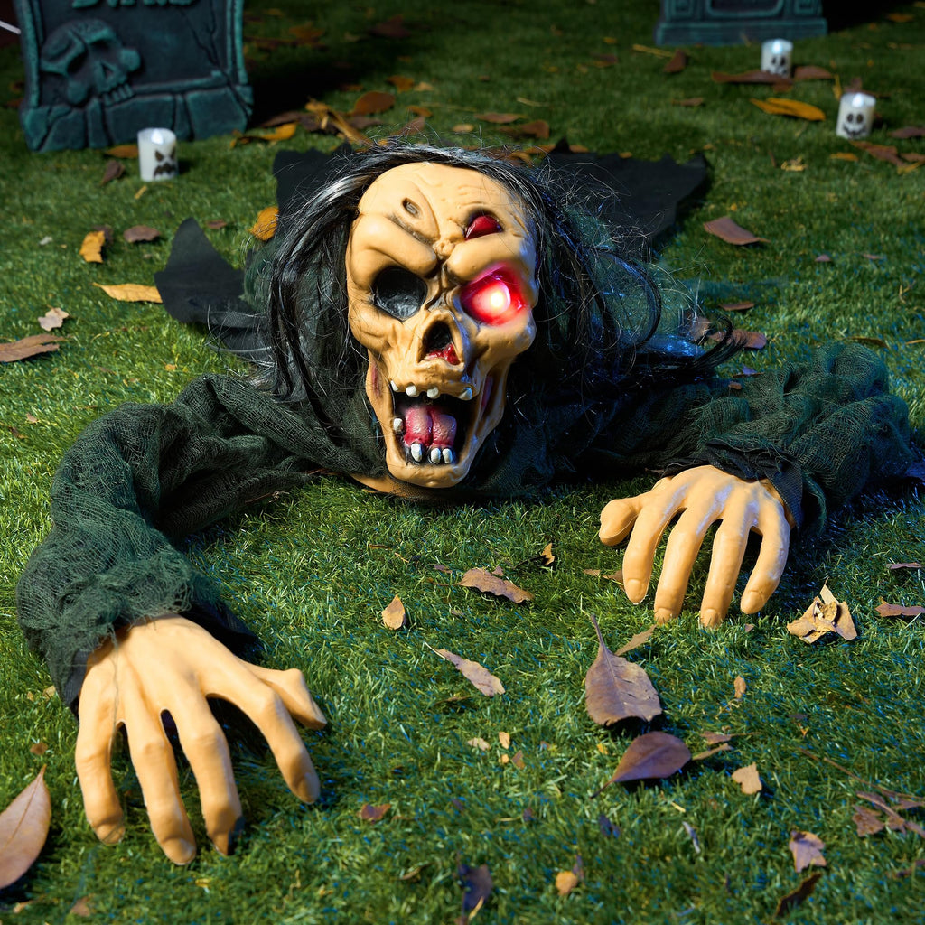Scary zombie groundbreaker prop with glowing red eye and open mouth, crawling on grass with fallen leaves and tombstones in background.