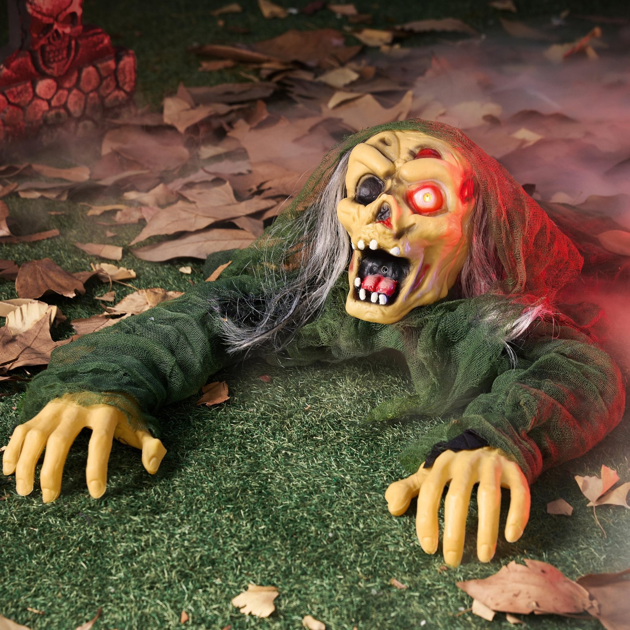 Scary zombie groundbreaker prop with glowing red eyes and open mouth, emerging from leaves on grass.
