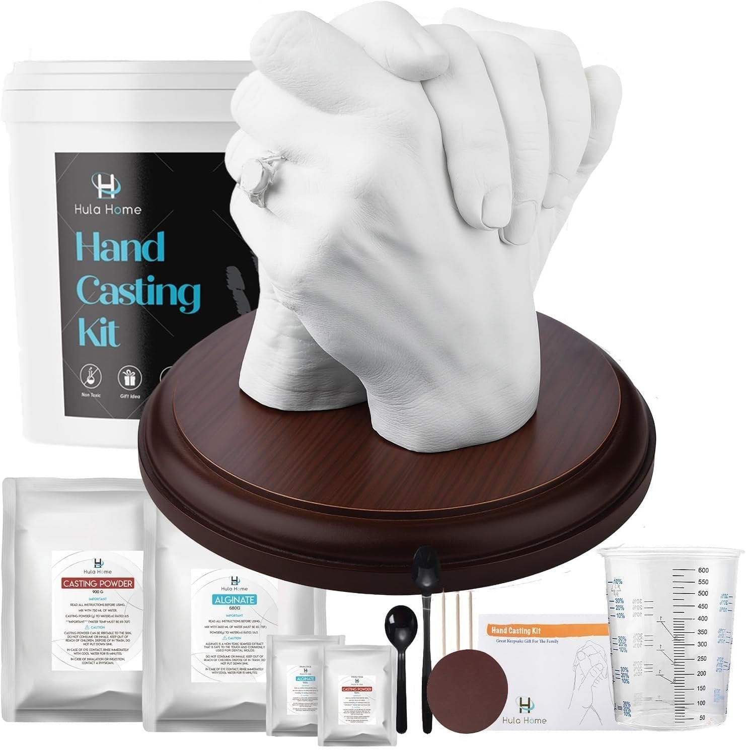 Hand casting kit with a finished sculpture of two hands on a wooden base, surrounded by kit components like powder bags, spoons, and a measuring cup.