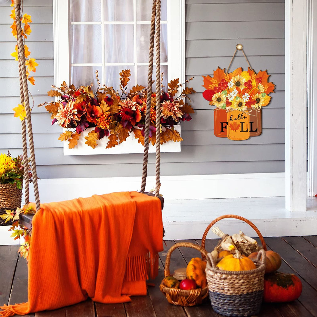 Front porch scene with a wooden door sign that says 'hello FALL' hanging next to a window box filled with autumn flowers and leaves. A swing with an orange blanket is in the foreground.