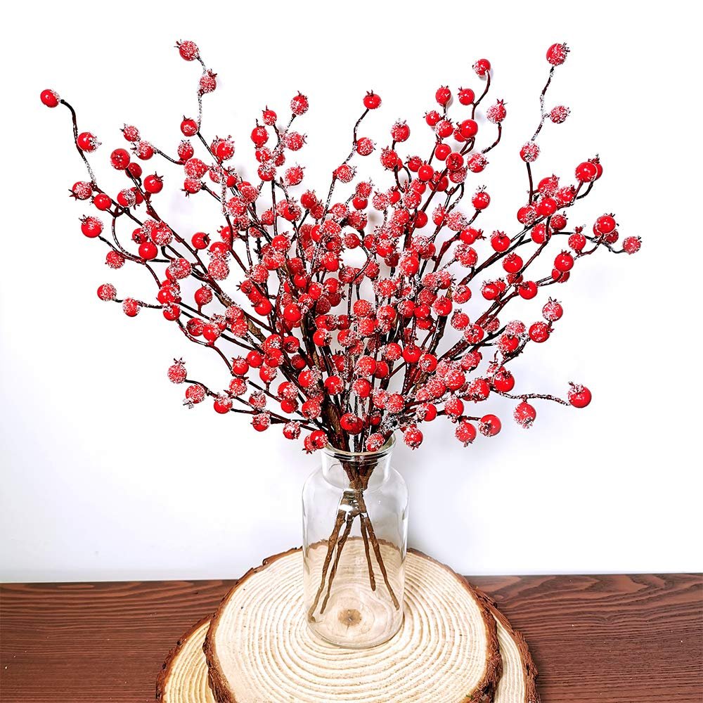 Artificial red berry sprays with frosted tips in a glass vase on a wooden slice