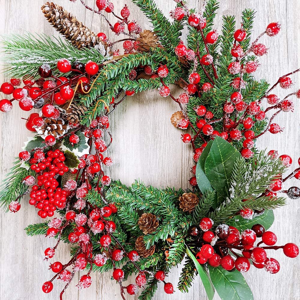 Close-up of a Christmas wreath with red berries, pinecones, and frosted pine needles on a light wood background.