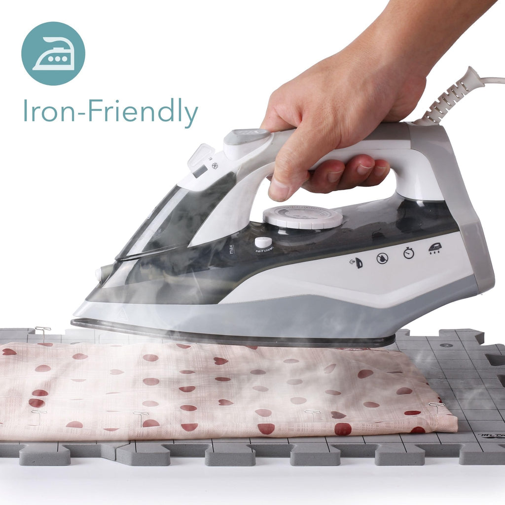 Hand holding an iron over fabric on interlocking blocking mats for knitting and crochet