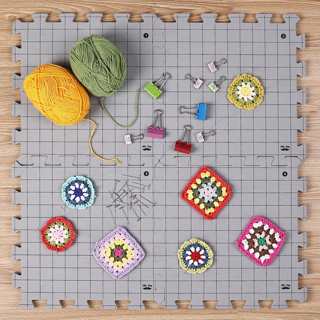 Interlocking blocking mats with yarn, crochet squares, T-pins, and binder clips on a wooden surface.