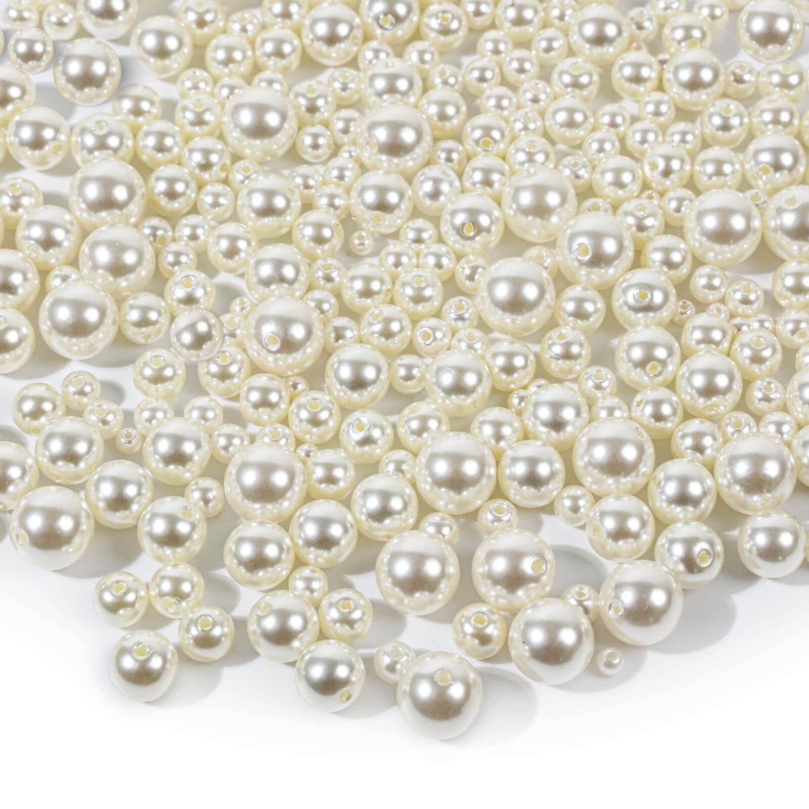 Ivory pearl craft beads in assorted sizes scattered on a white background.