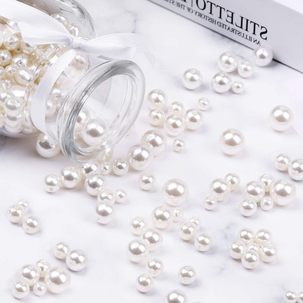 Ivory pearl craft beads in assorted sizes spilling from a glass jar tied with a white ribbon.