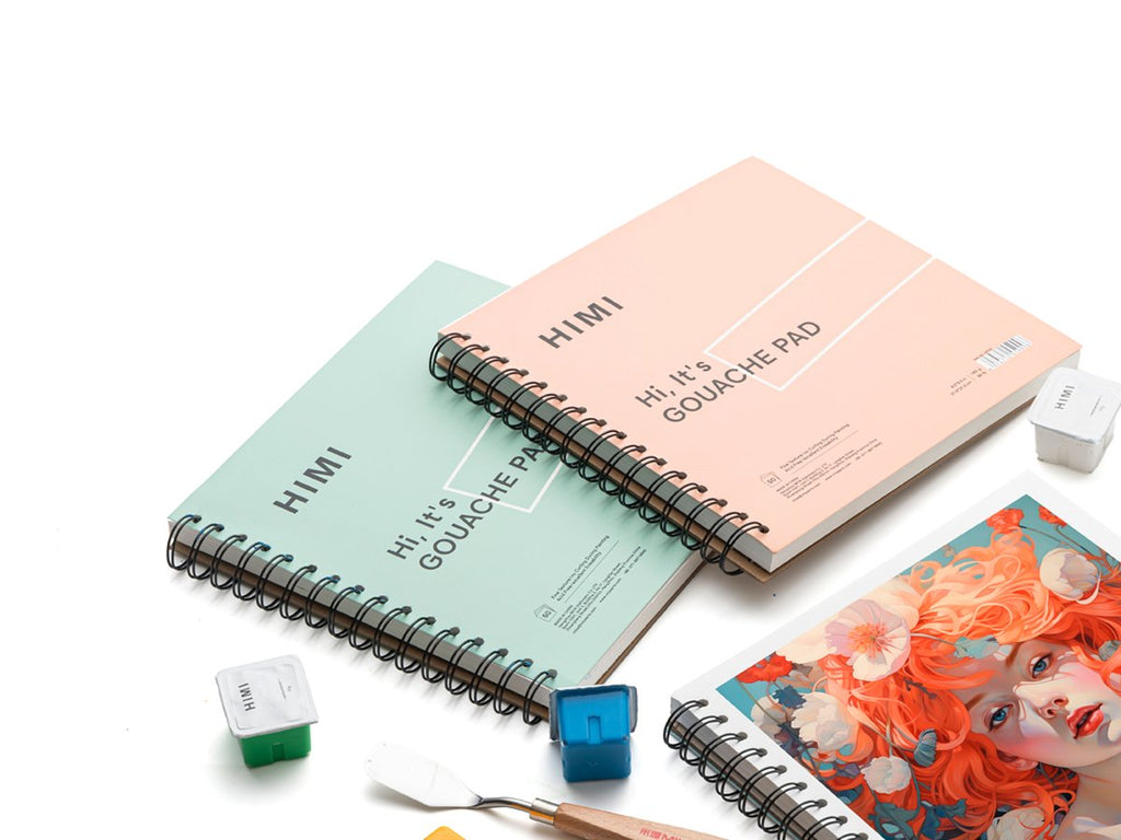 Two spiral-bound gouache paint pads, one pink and one teal, with small paint pots and a palette knife on a white background.
