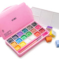 Pink case with 18 colors of gouache paint, palette, and brushes, with individual paint pots and extra paint pots scattered around.
