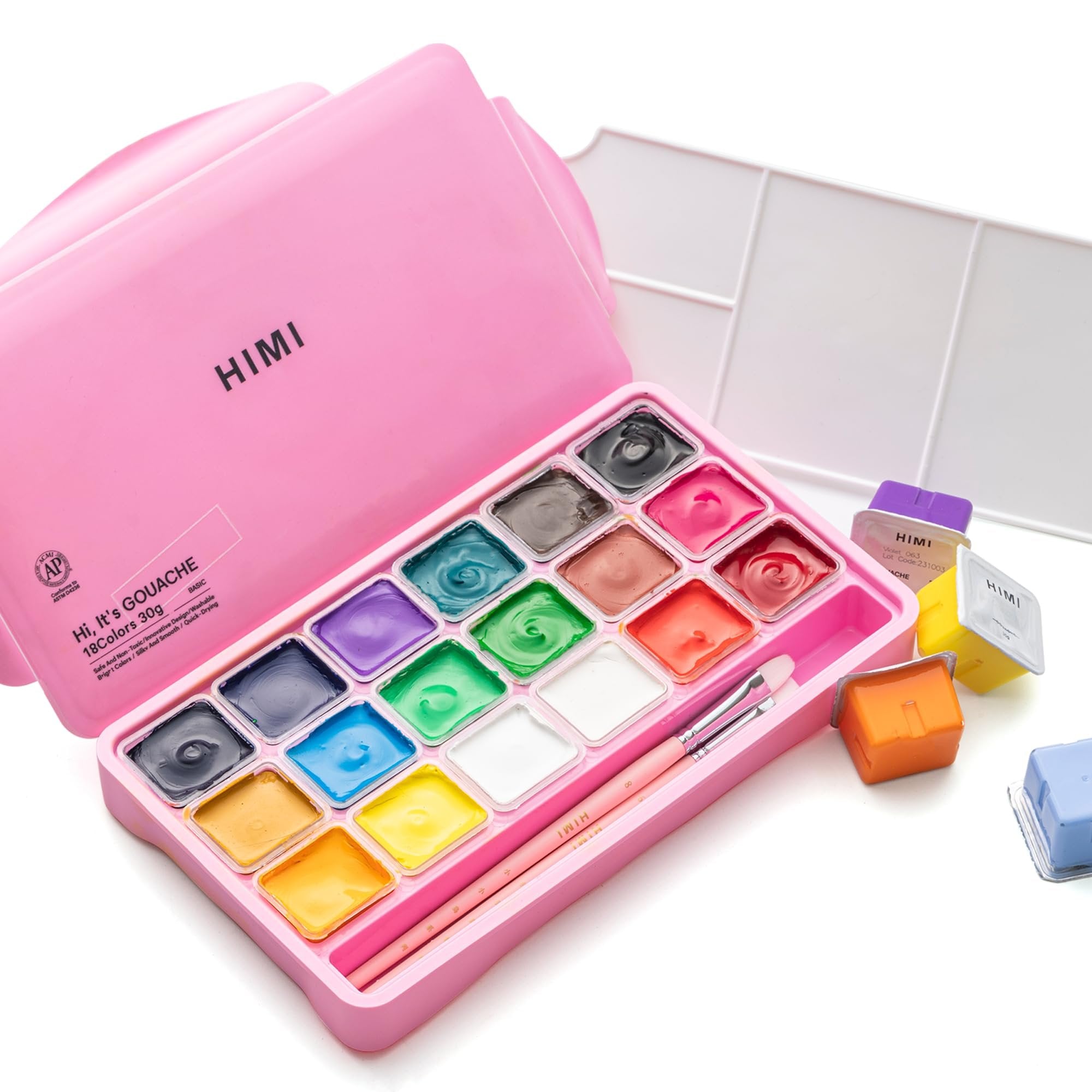 Pink case with 18 colors of gouache paint, palette, and brushes, with individual paint pots and extra paint pots scattered around.