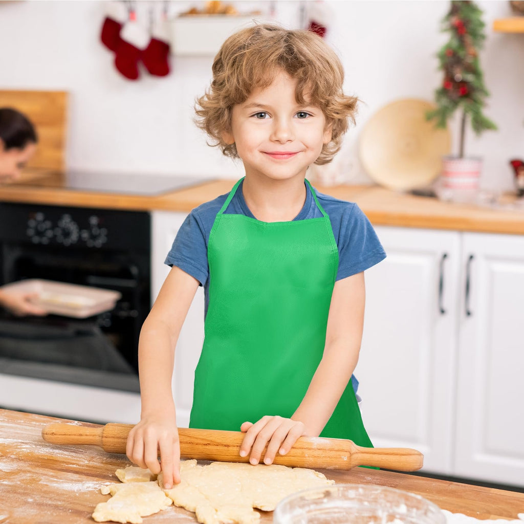 Young boy wearing a green apron rolls out dough in a kitchen setting with Christmas decorations.