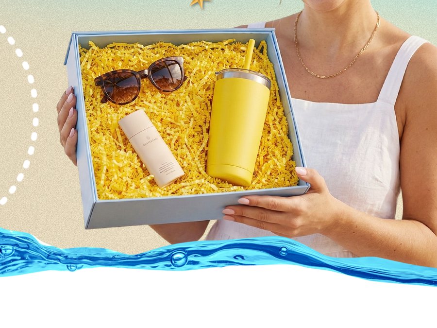 Woman holding a gift box filled with yellow crinkle paper, sunglasses, and a yellow tumbler with a straw.