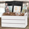 White wooden crate filled with crinkle cut paper shred and various tea packages and jars.