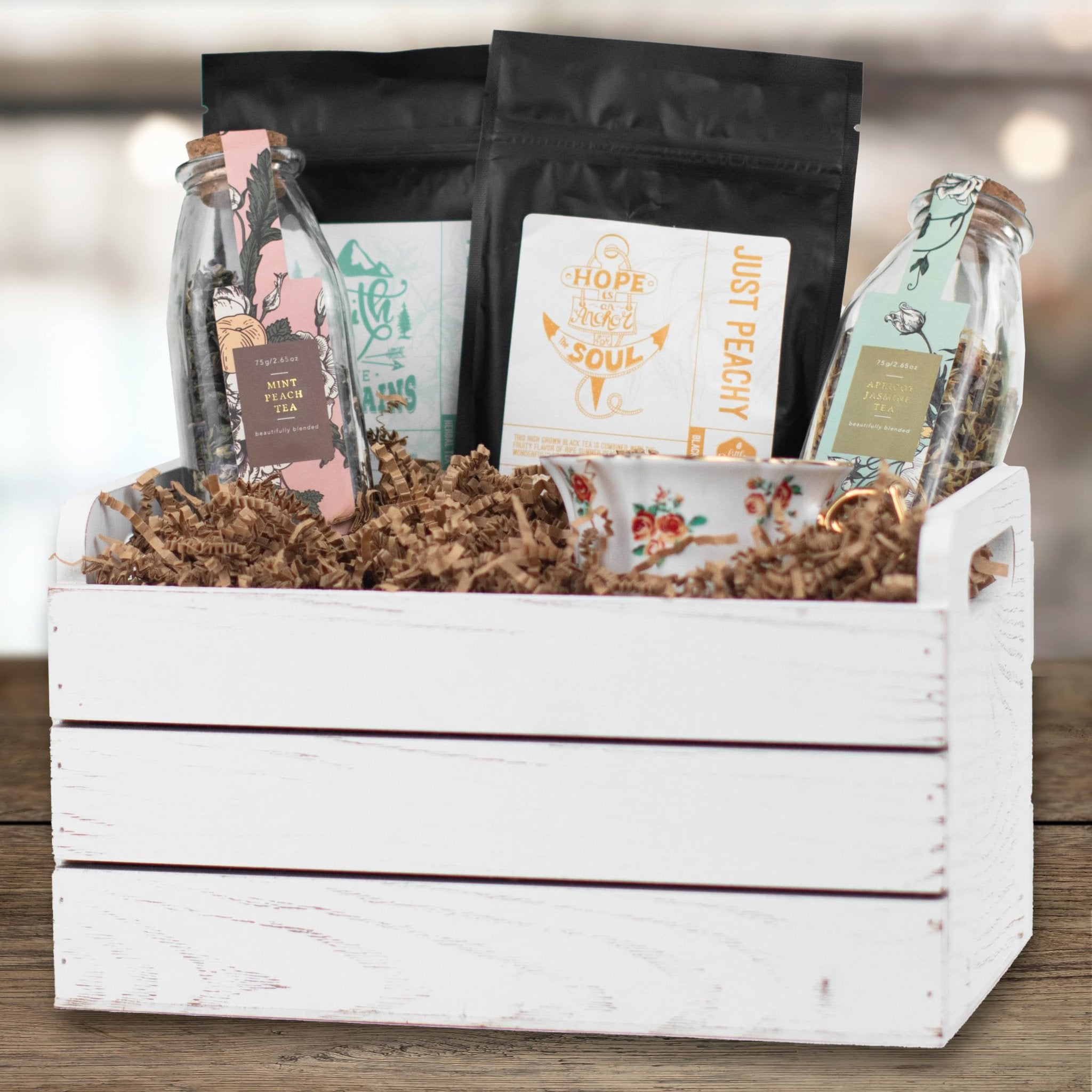 White wooden crate filled with crinkle cut paper shred and various tea packages and jars.