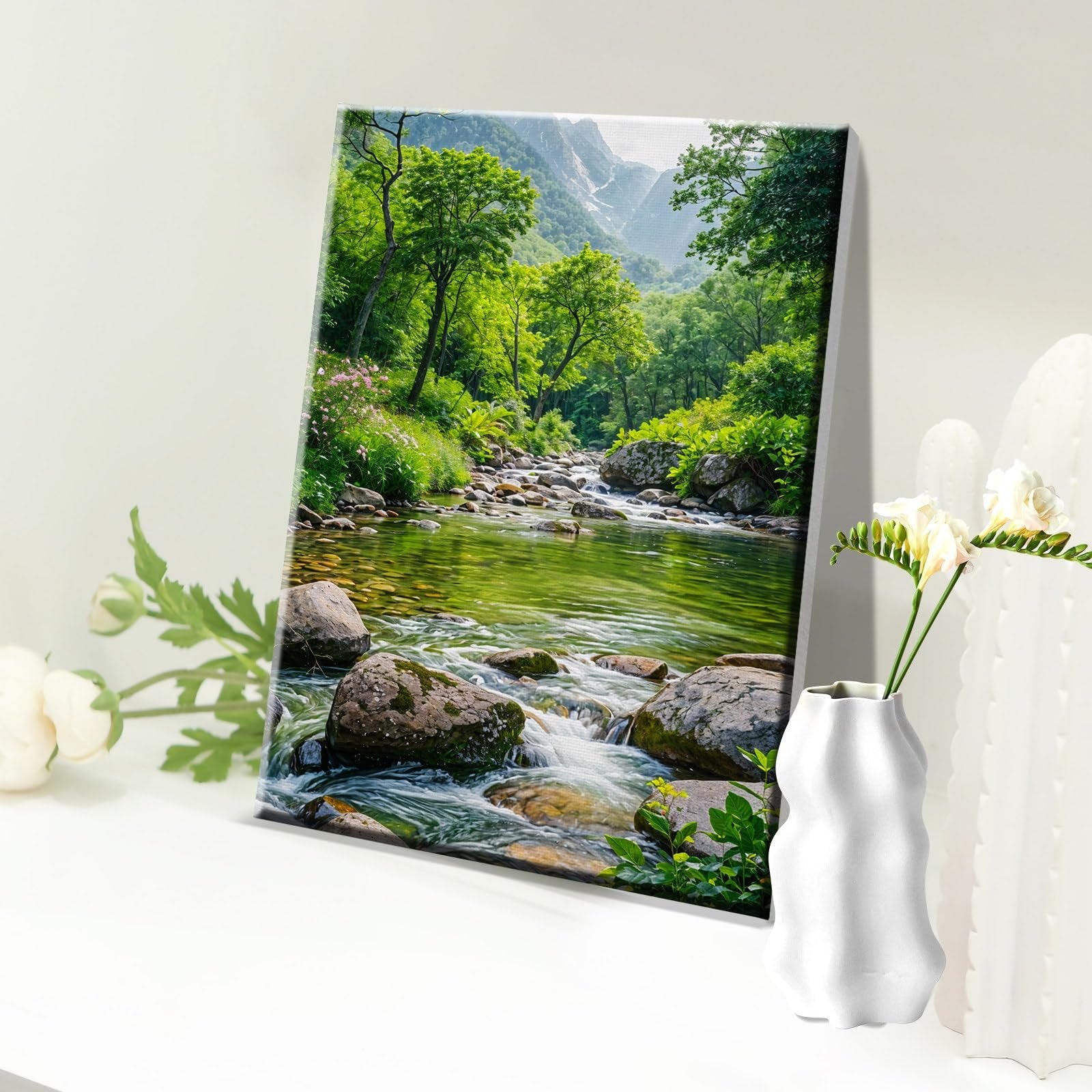 Framed canvas print of a vibrant green forest landscape with a rocky river flowing through it, mountains in the background.