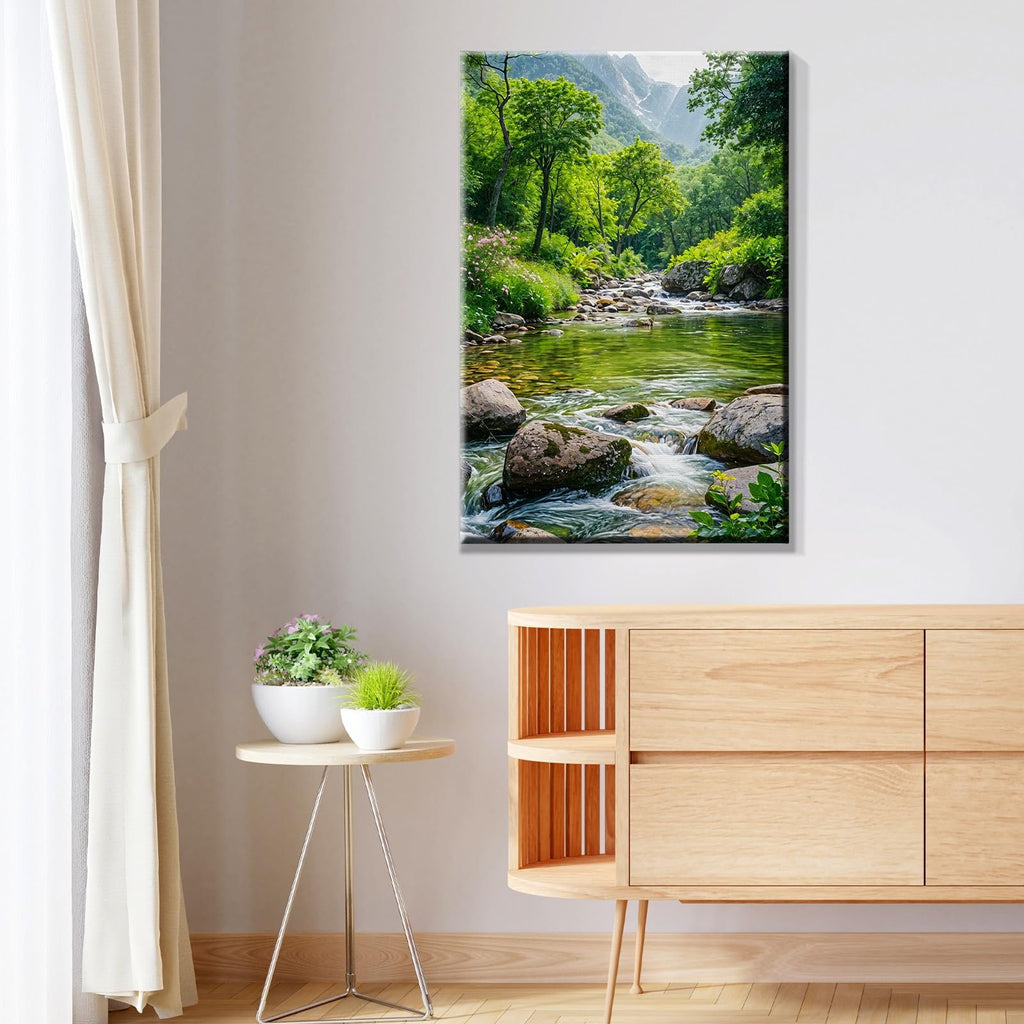 Framed landscape painting of a stream flowing through a forest with mountains in the background, displayed on a wall.