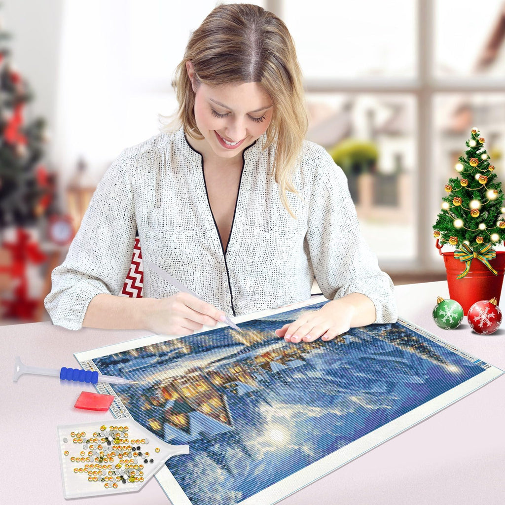 Woman working on a large diamond art kit depicting a winter village scene with Christmas decorations